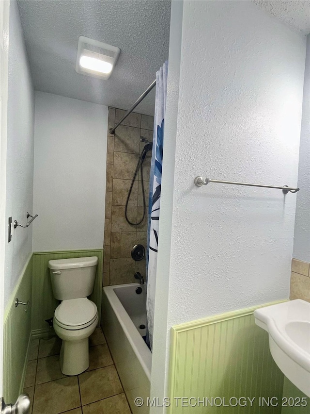 bathroom with tile patterned floors, shower / bathtub combination with curtain, a textured ceiling, and toilet