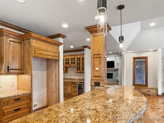 kitchen featuring light stone countertops, decorative backsplash, decorative light fixtures, ornamental molding, and beverage cooler