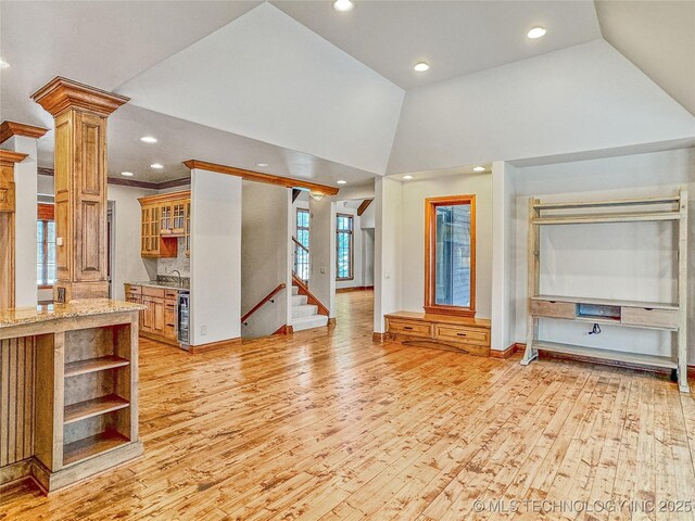 unfurnished living room featuring wine cooler, sink, light hardwood / wood-style floors, high vaulted ceiling, and decorative columns