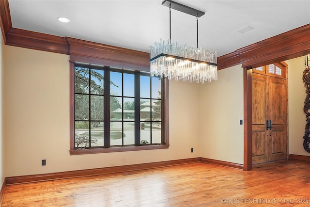 unfurnished dining area with ornamental molding, a chandelier, and light wood-type flooring