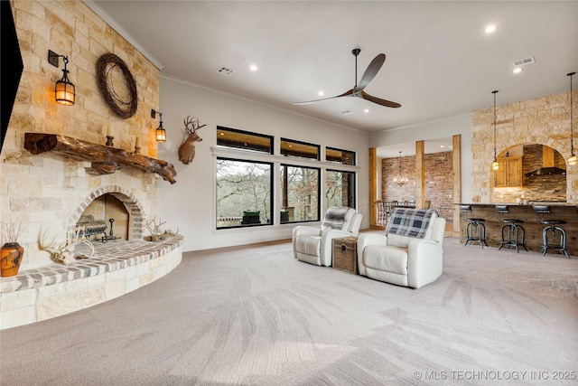 unfurnished living room featuring ceiling fan, carpet, crown molding, and a stone fireplace