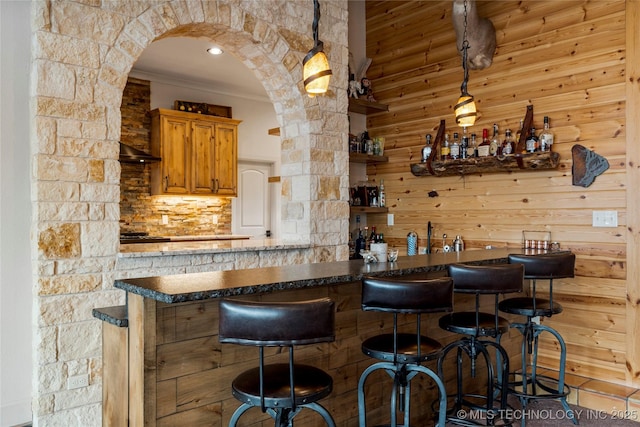 bar with decorative backsplash, hanging light fixtures, crown molding, and range hood