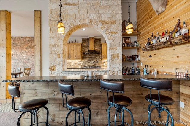 bar featuring decorative light fixtures, wall chimney exhaust hood, and wooden walls