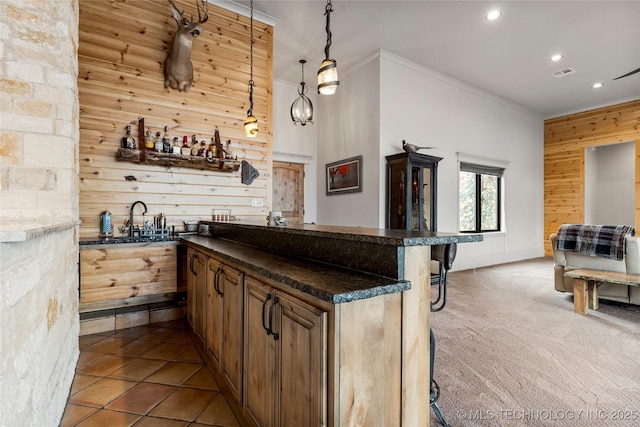 bar with carpet, dark stone counters, hanging light fixtures, wood walls, and crown molding