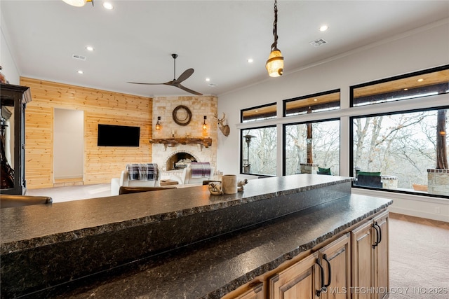 kitchen with decorative light fixtures, ceiling fan, a fireplace, wood walls, and light carpet