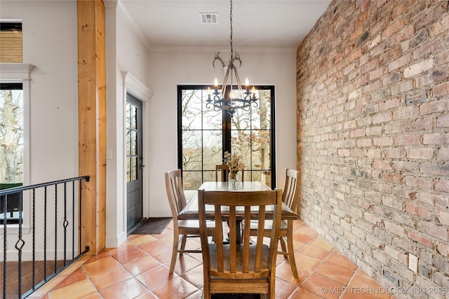 tiled dining area featuring a wealth of natural light, brick wall, ornamental molding, and a chandelier