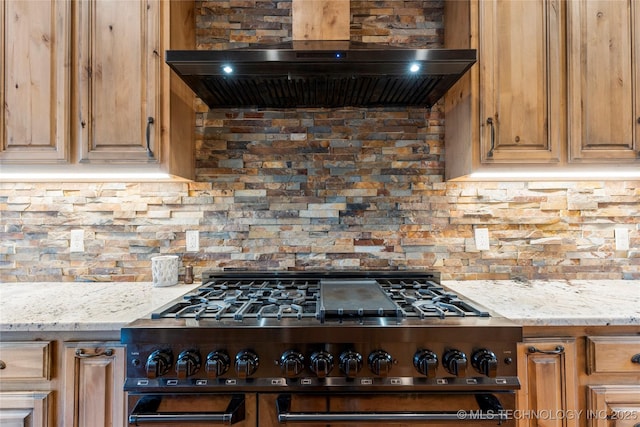 kitchen featuring high end stainless steel range, stovetop, backsplash, light stone counters, and range hood