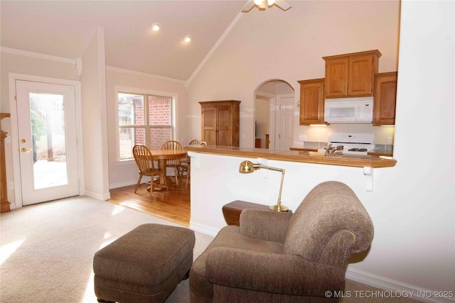 kitchen with a breakfast bar, high vaulted ceiling, ornamental molding, stove, and kitchen peninsula