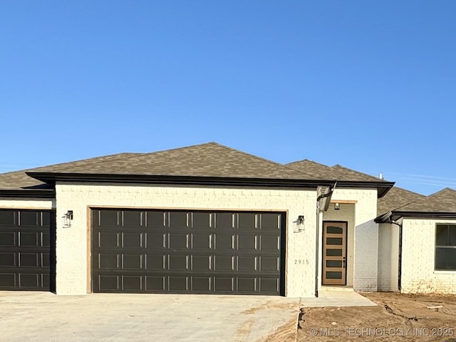 view of front facade featuring a garage, concrete driveway, and roof with shingles