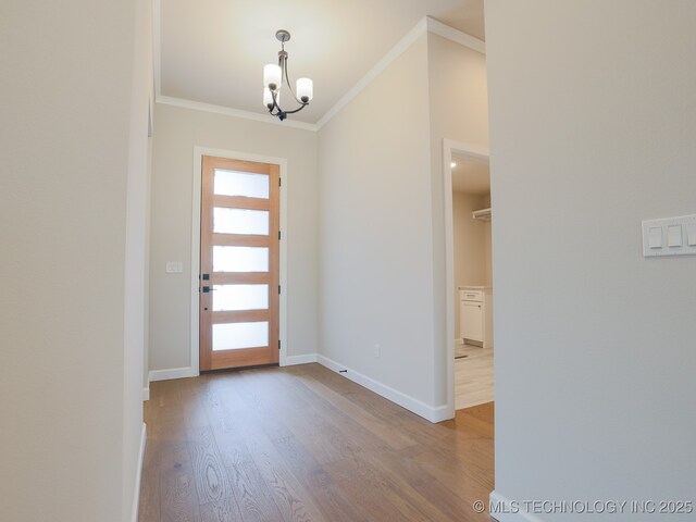 foyer entrance with baseboards, ornamental molding, wood finished floors, and a chandelier