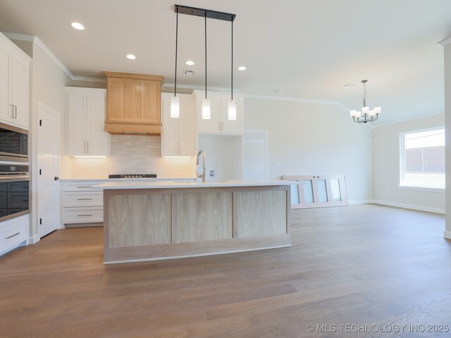kitchen featuring ornamental molding, a center island with sink, a chandelier, appliances with stainless steel finishes, and backsplash