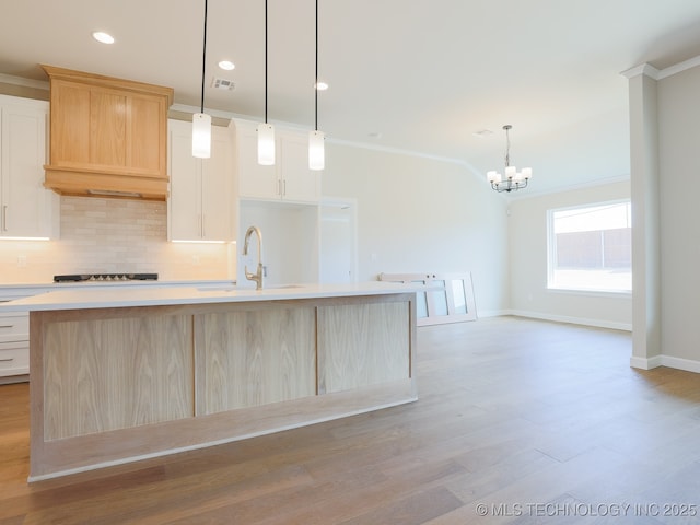 kitchen featuring a sink, light countertops, ornamental molding, decorative backsplash, and a center island with sink