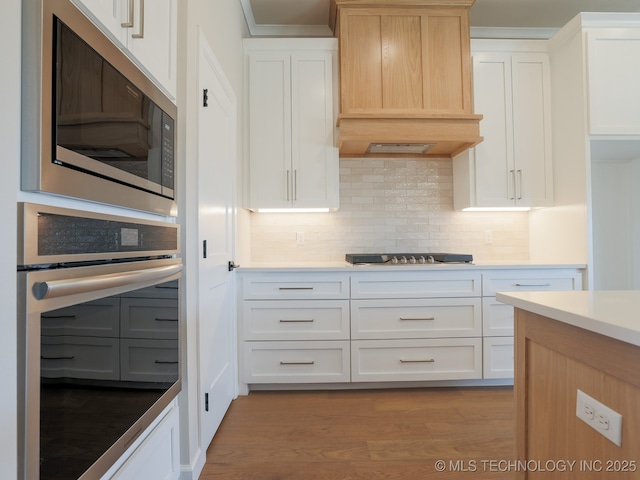 kitchen with backsplash, custom range hood, light countertops, light wood finished floors, and stainless steel appliances