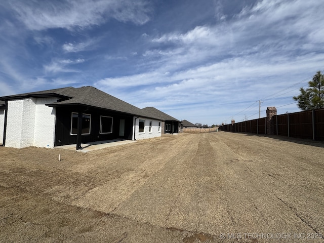 view of home's exterior featuring a patio area, a shingled roof, and fence