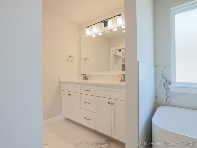 bathroom featuring double vanity, marble finish floor, a freestanding tub, baseboards, and a sink