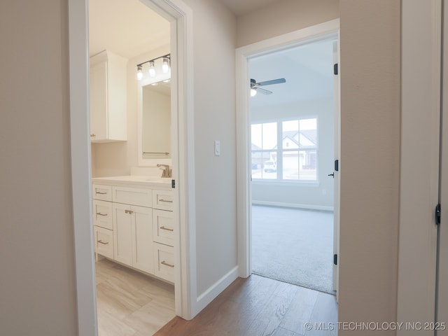 corridor with a sink, baseboards, and light wood-style floors