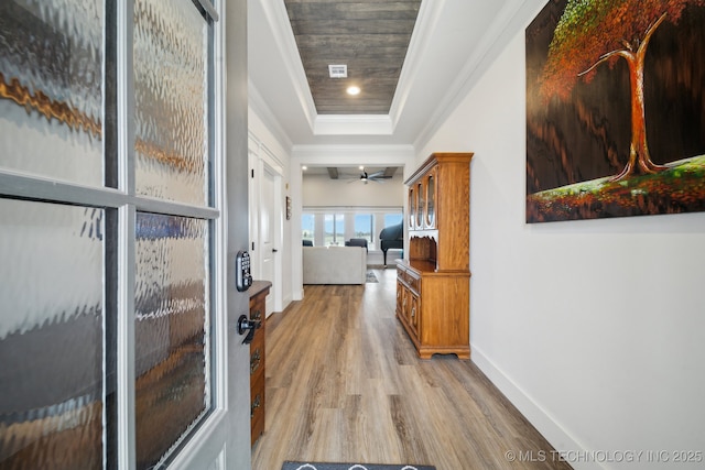 hallway with light wood-type flooring, ornamental molding, wood ceiling, and a raised ceiling