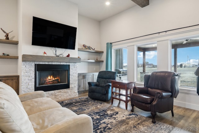 living room featuring light hardwood / wood-style floors, built in features, beam ceiling, and a stone fireplace