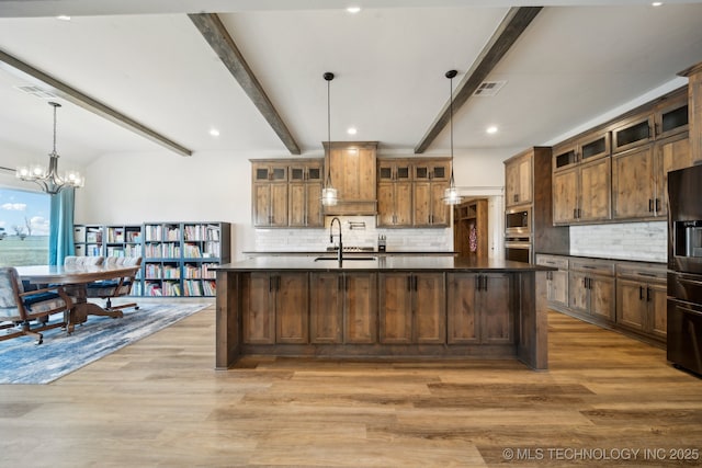 kitchen featuring hardwood / wood-style floors, a kitchen island with sink, decorative light fixtures, beam ceiling, and sink