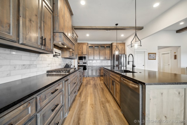 kitchen featuring pendant lighting, stainless steel appliances, beamed ceiling, sink, and a center island with sink