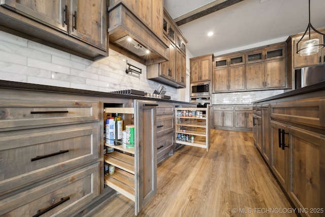 kitchen featuring stainless steel microwave, decorative light fixtures, tasteful backsplash, hardwood / wood-style floors, and custom exhaust hood