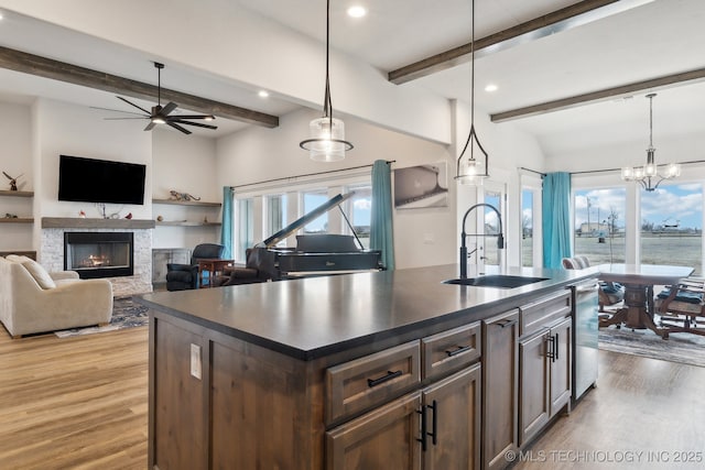 kitchen featuring decorative light fixtures, a fireplace, a center island with sink, beamed ceiling, and sink