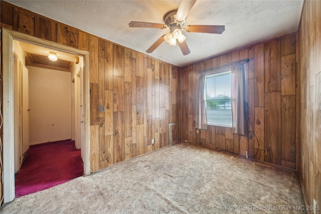 carpeted spare room with ceiling fan, a textured ceiling, and wood walls