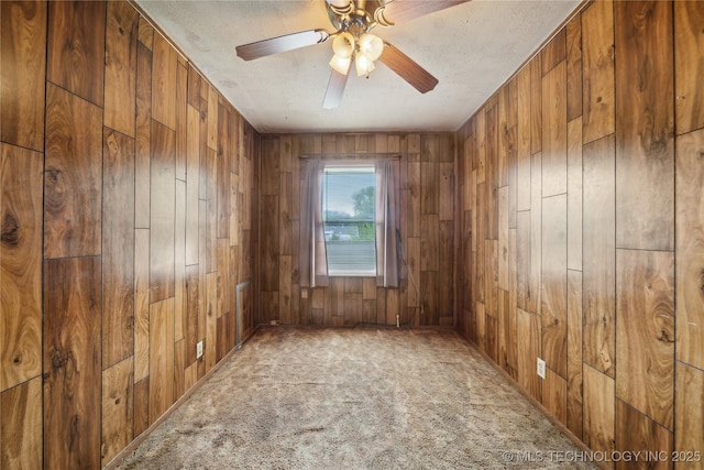 carpeted spare room featuring ceiling fan, wood walls, and a textured ceiling