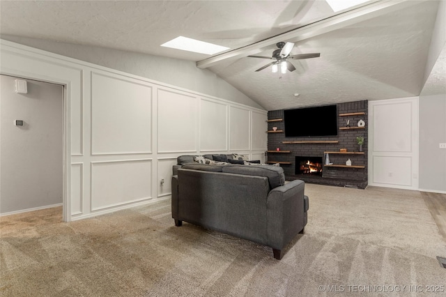 living room featuring light carpet, a brick fireplace, a textured ceiling, ceiling fan, and vaulted ceiling with skylight