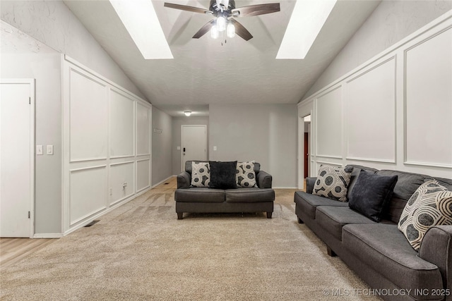 living room featuring light carpet, lofted ceiling with skylight, and ceiling fan