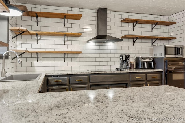 kitchen featuring sink, decorative backsplash, light stone counters, black appliances, and wall chimney exhaust hood