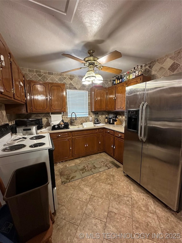 kitchen with electric stove, ceiling fan, stainless steel refrigerator with ice dispenser, sink, and a textured ceiling