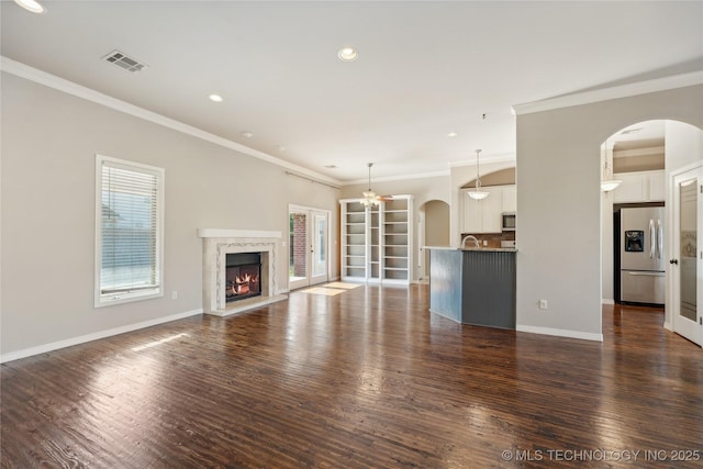 unfurnished living room with dark wood-type flooring, a premium fireplace, ornamental molding, and ceiling fan