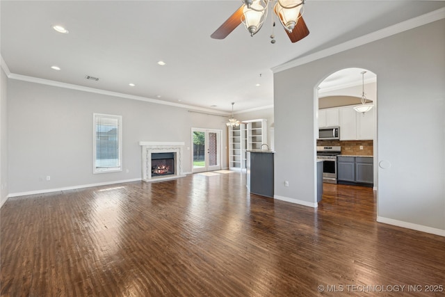 unfurnished living room with dark wood-type flooring, a premium fireplace, ceiling fan with notable chandelier, and ornamental molding