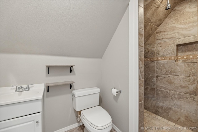 bathroom featuring a tile shower, vanity, lofted ceiling, and toilet