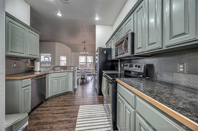 kitchen with stainless steel appliances, sink, hanging light fixtures, dark hardwood / wood-style floors, and a notable chandelier