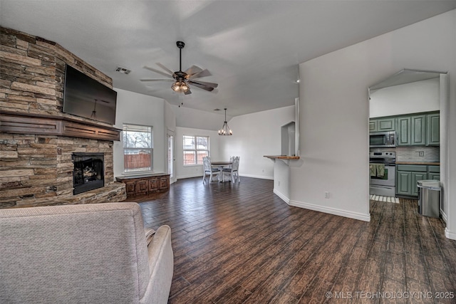 unfurnished living room with ceiling fan with notable chandelier, dark wood-type flooring, lofted ceiling, and a stone fireplace