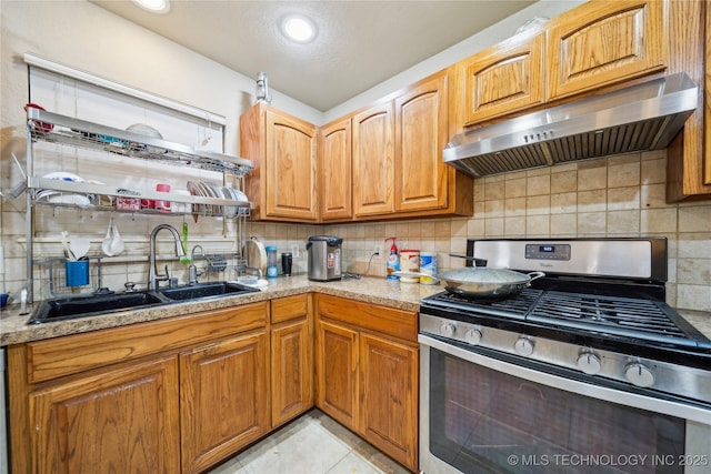 kitchen featuring tasteful backsplash, stainless steel range with gas stovetop, range hood, light countertops, and a sink