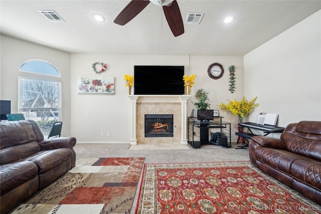 living room featuring a tile fireplace, light carpet, visible vents, and a textured ceiling