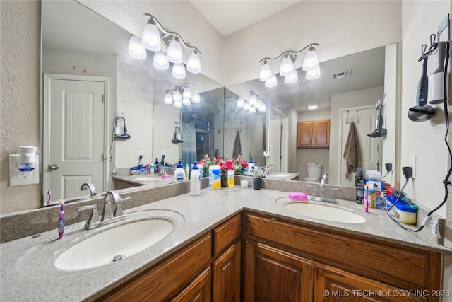 bathroom featuring toilet, double vanity, a sink, and visible vents