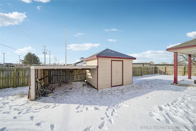 snow covered structure with an outbuilding, a storage shed, and a fenced backyard