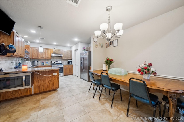 kitchen with under cabinet range hood, stainless steel appliances, a peninsula, visible vents, and hanging light fixtures