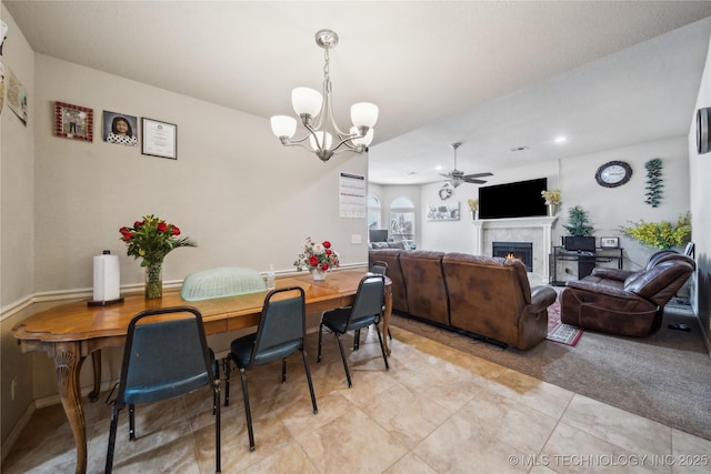 dining area featuring a lit fireplace, baseboards, and ceiling fan with notable chandelier