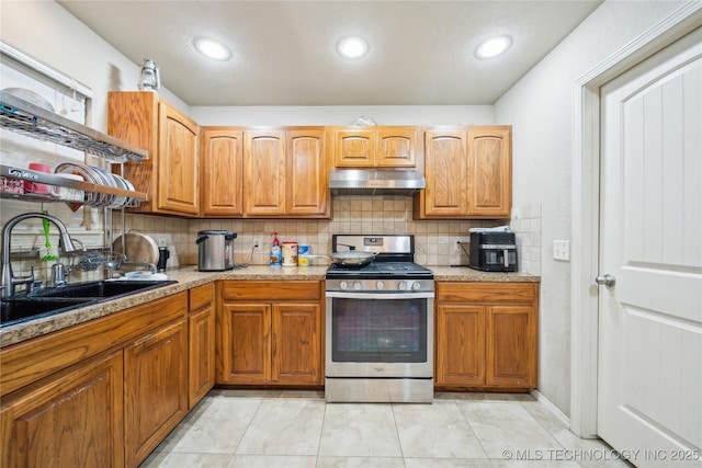 kitchen featuring tasteful backsplash, brown cabinets, stainless steel gas range, under cabinet range hood, and a sink