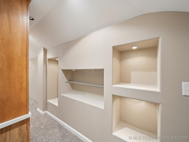 hallway featuring carpet, built in shelves, and lofted ceiling