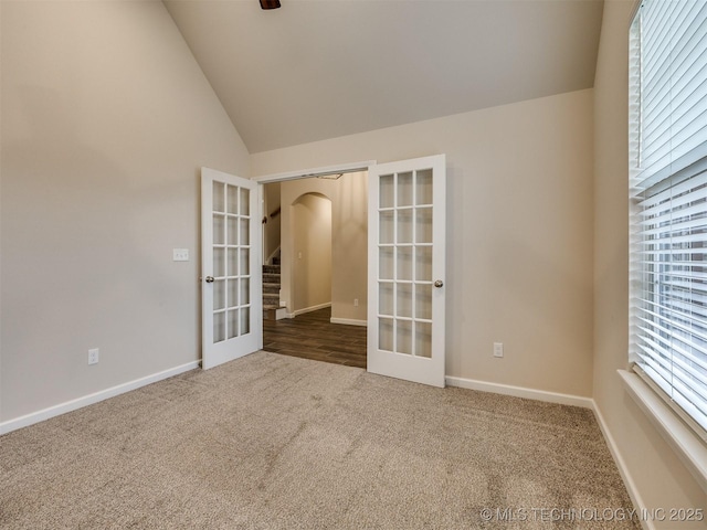 carpeted spare room featuring lofted ceiling and french doors