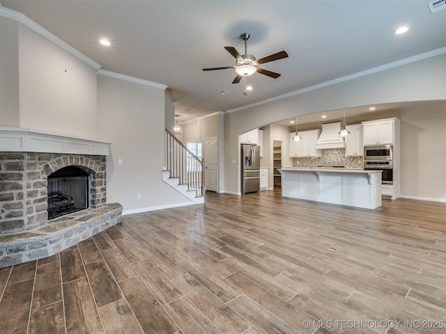 unfurnished living room featuring ceiling fan, ornamental molding, and a stone fireplace