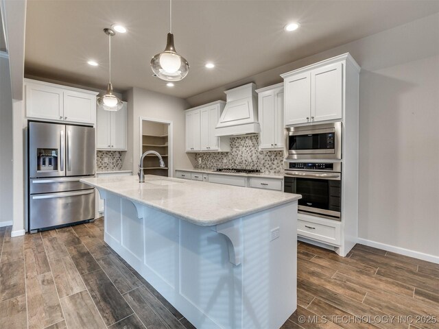 kitchen with custom exhaust hood, white cabinets, appliances with stainless steel finishes, and pendant lighting