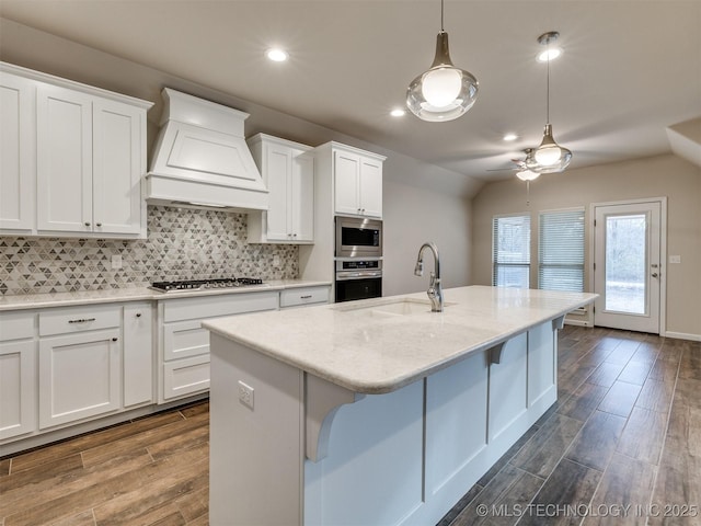 kitchen with a center island with sink, appliances with stainless steel finishes, white cabinetry, and custom range hood