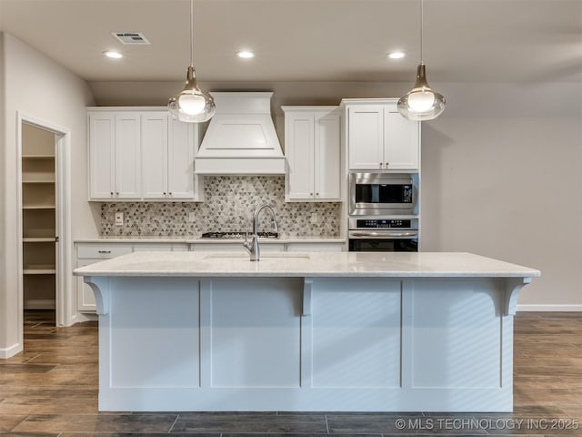 kitchen with appliances with stainless steel finishes, custom exhaust hood, white cabinetry, and light stone counters